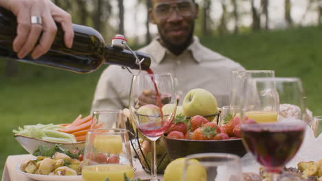 nahaufnahme eines nicht erkennbaren mannes, der während einer party im freien mit seinen freunden rotwein in ein glas gießt