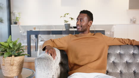 relaxing on sofa, african american man smiling and looking away in modern living room, at home