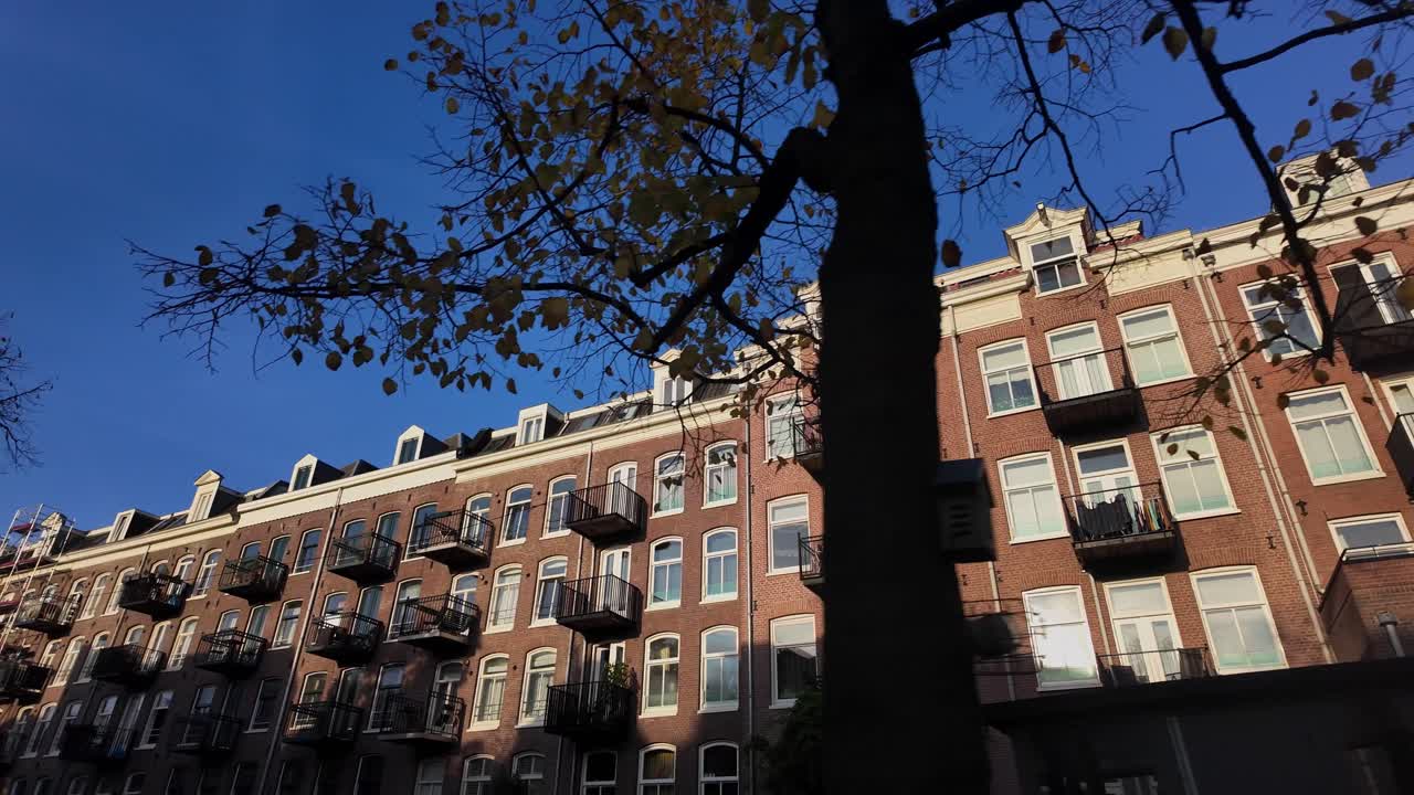 Plano de deslocamento lateral em ângulo baixo de edifícios de apartamentos residenciais de tijolos com varandas e árvores de outono no bairro de Amsterdam
