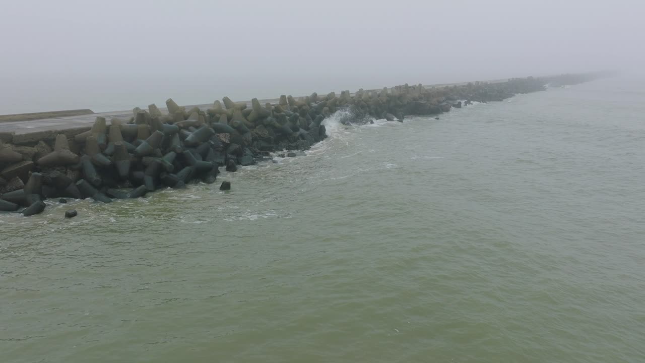 리파자 콘크리트 부두 항구, 발트해 해안선, 짙은 안개가 낀 안개 낀 날, 변덕스러운 느낌, 큰 폭풍우 파도가 튀고, 앞으로 나아가는 넓은 오름차순 드론 샷