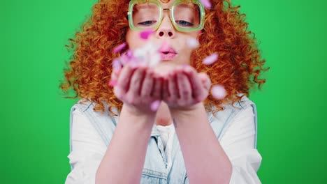 young happy woman blowing colorful confetti to camera and smiling, green chroma key background, slow motion