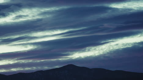 silhouette of mountains with clouds passing in winter time lapse