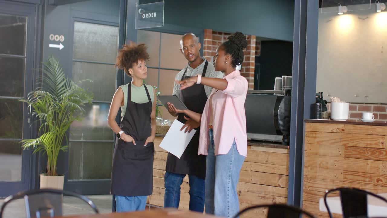 Afroamerikansk cafépersonale stimler sammen om en tablet, peger på områder ved disken og planlægger opgaver.