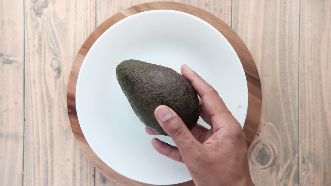 나무 테이블 위 에 있는  그 에 아보카도 를 들고 있는 손