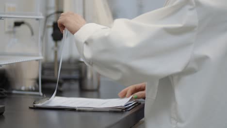 white coat female scientist in lab reading through research notes on a clipboard