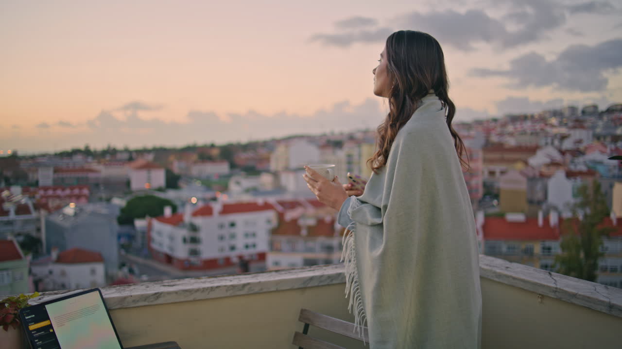 Ragazza rilassata che ammira il paesaggio urbano al tramonto da una terrazza, in primo piano. Donna che scatta una foto.