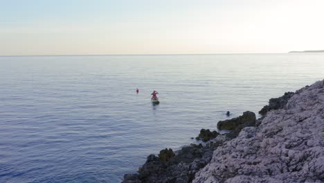 girl sitting and rowing kayak with a man swimming near the rocky coast of losinj island in croatia