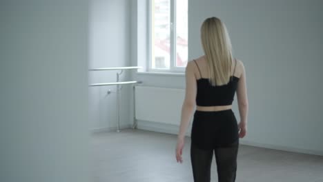 fit girl in black clothes performing contemporary. female dancer shows flowing motions, body and hands waves at white room. modern ballet dance choreography. young woman is moving smoothly