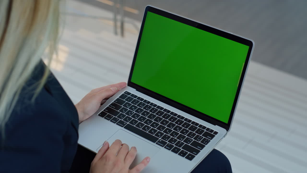 Primo piano di mani femminili che utilizzano un touchpad su uno schermo verde di un laptop in un ambiente aziendale