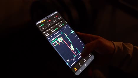 Eine-Person-Analysiert-Kryptowährungsdiagramme-Auf-Einem-Smartphone-Bei-Schwachem-Licht
