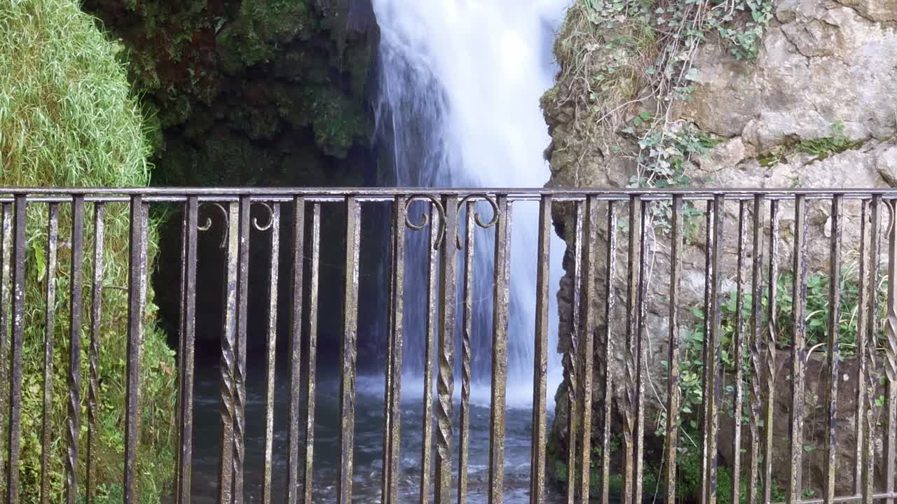 barandilla de protección de metal con una idílica cascada rural que fluye en el fondo