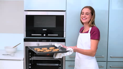 blonde woman taking cookies in oven in kitchen