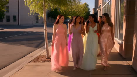 a group of women in elegant dresses walking and smiling on a sidewalk