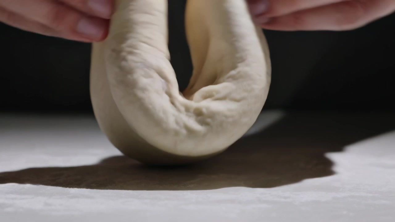 Mani esperte che premono il palmo, levigano, allungano e piegano l'impasto lievitato sul bancone di una panetteria per formare un anello.