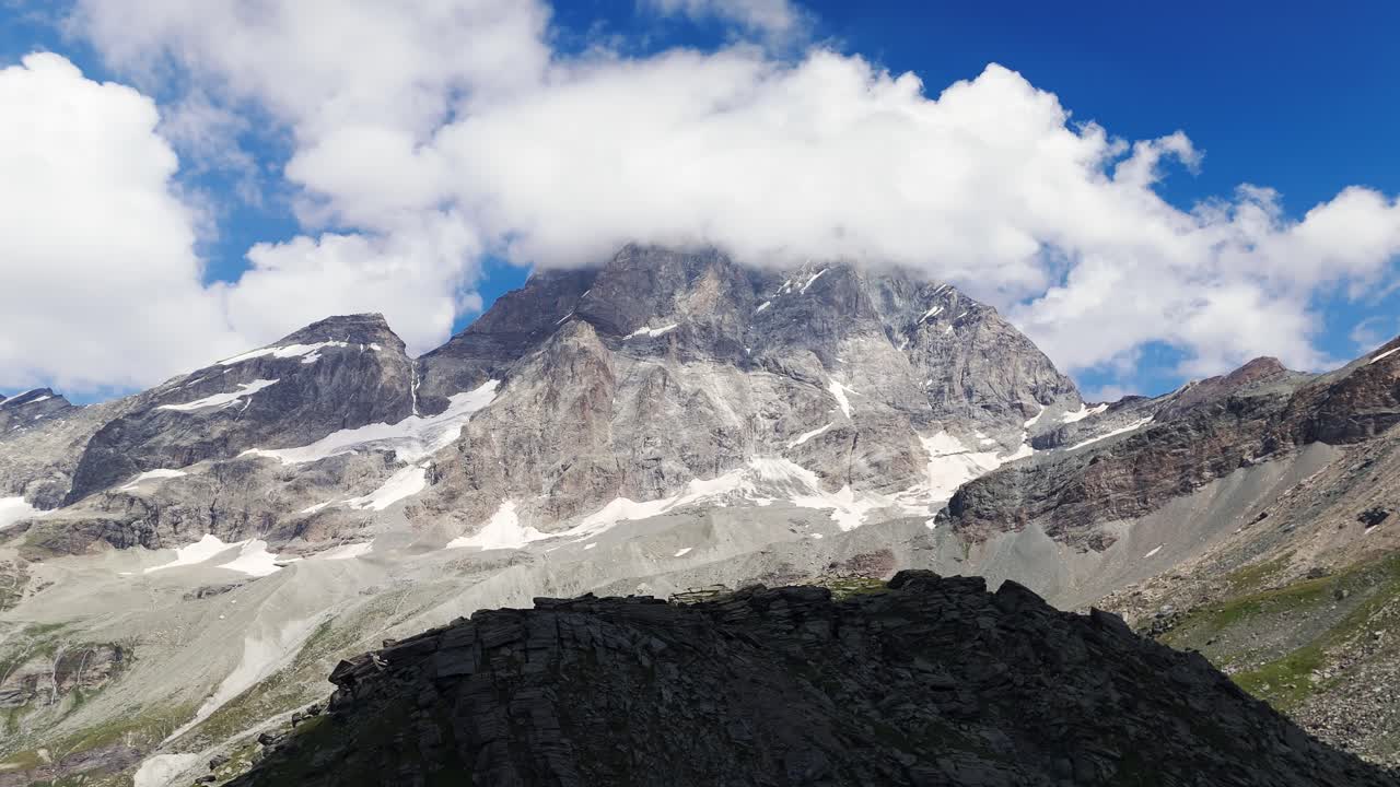 Aerial shot pulling back to reveal a mountain silhouette against the setting sun in Cervinia, Italy