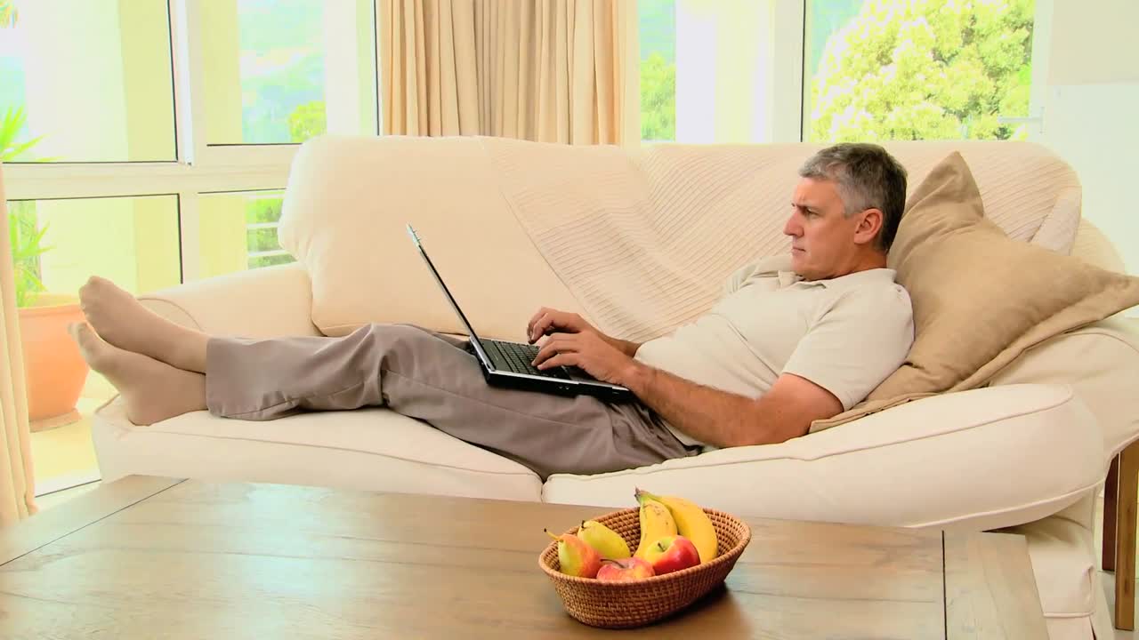 Man lying on sofa while working