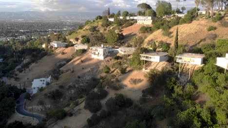 aerial flyby of homes on stilts hanging off cliffs of a mountain overlooking a valley city