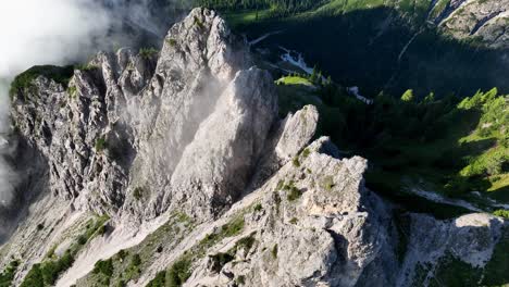 top down aerial view spiraling over several rocky jagged peaks in the dolomites on a partly foggy summer day