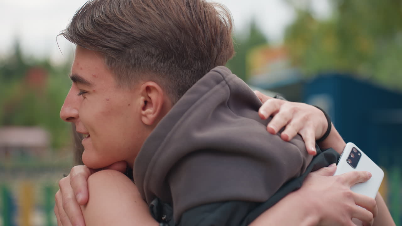 primo piano di un'adolescente bianca sorpresa da un ammiratore segreto in un parco che cattura un sorriso timido e un abbraccio veloce, telefono visibile durante l'abbraccio, luce naturale soffusa e sfondo con recinzione che amplificano la riunione intima e sincera