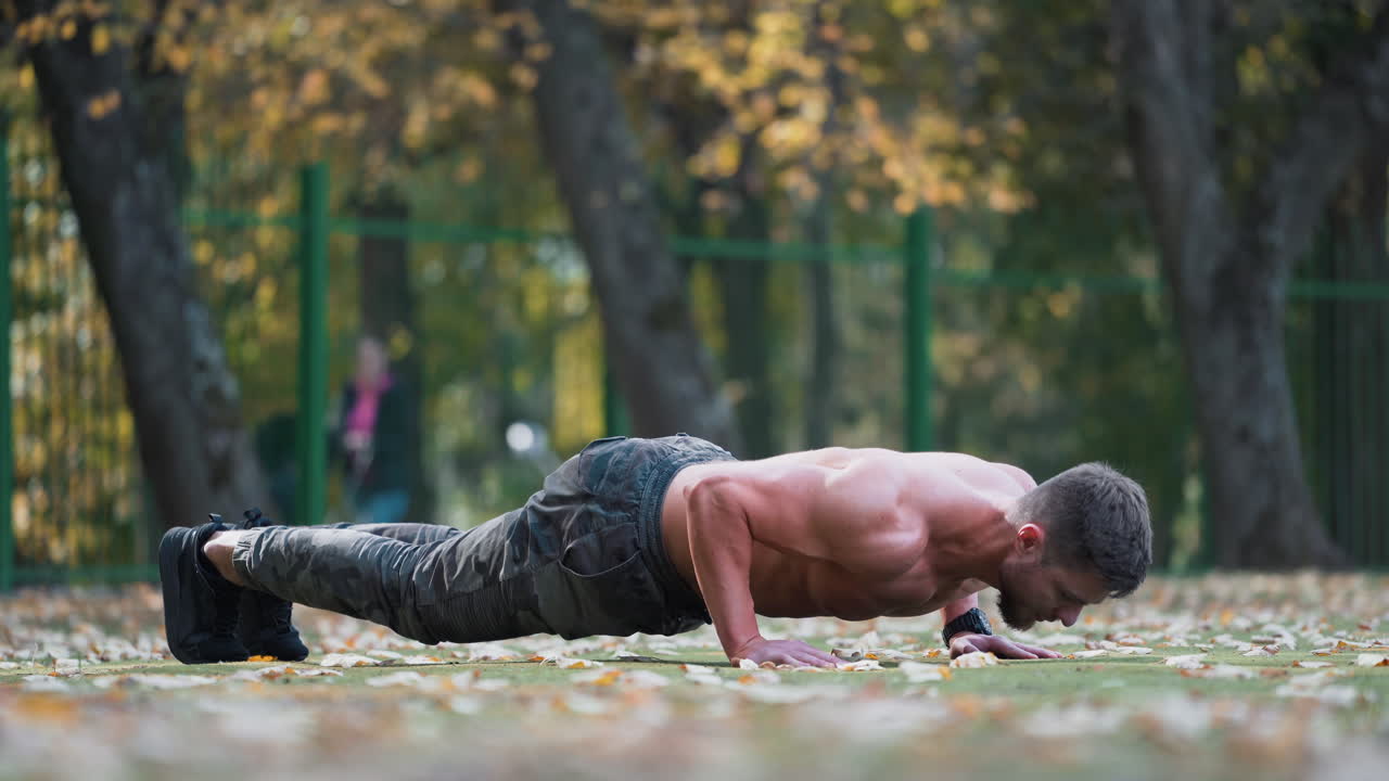 Sportsman doing push- ups exercise outdoors. Shirtless fitness man doing push-ups on the ground. Athletic man doing workout in autumn.