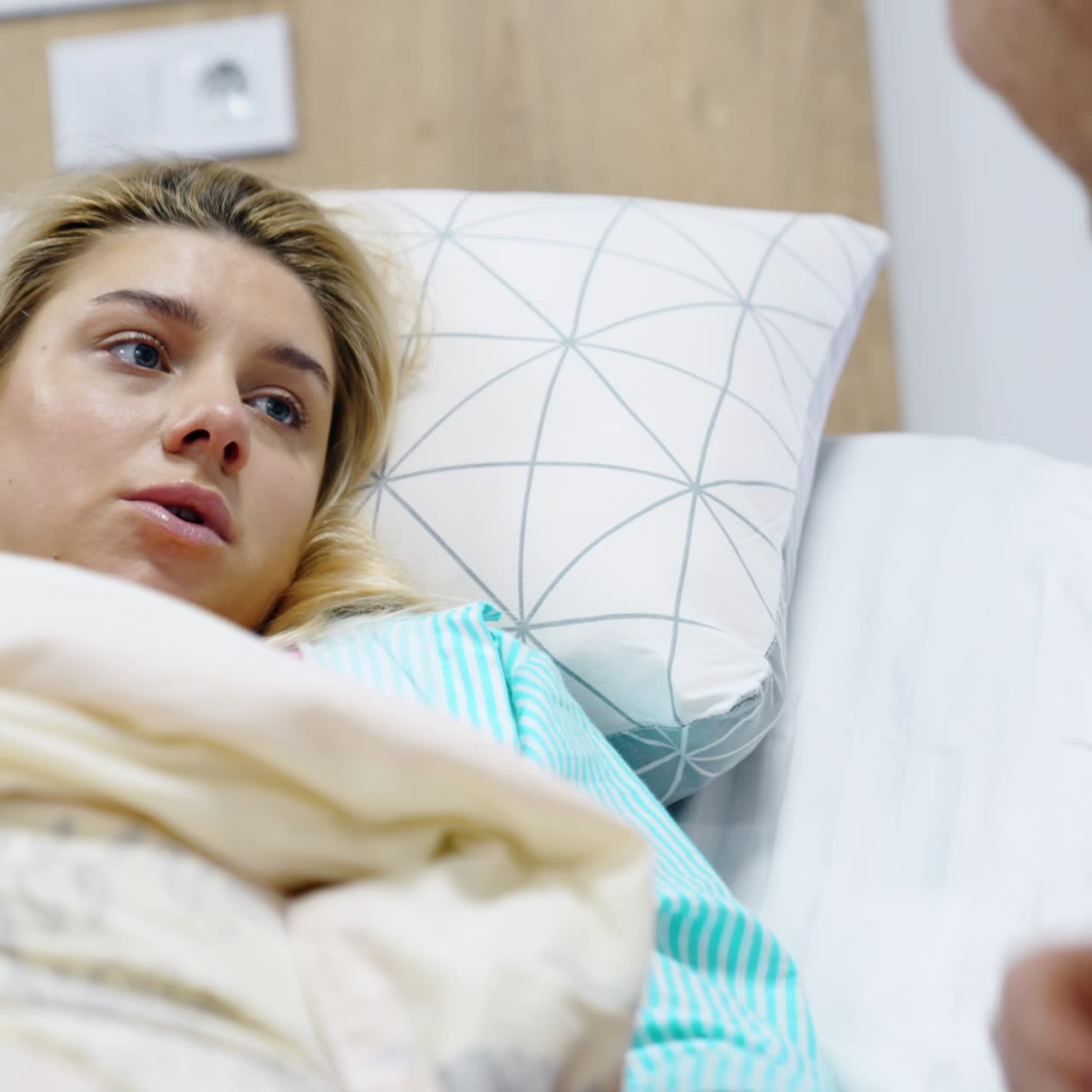 Caucasian man kissing his wife's hand who lies in the hospital bed. Husband tries to sooth woman before the labour. Close up