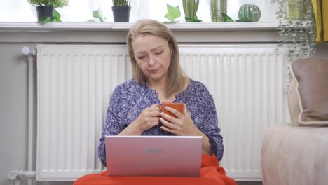 cold woman at home drinking coffee and using laptop.