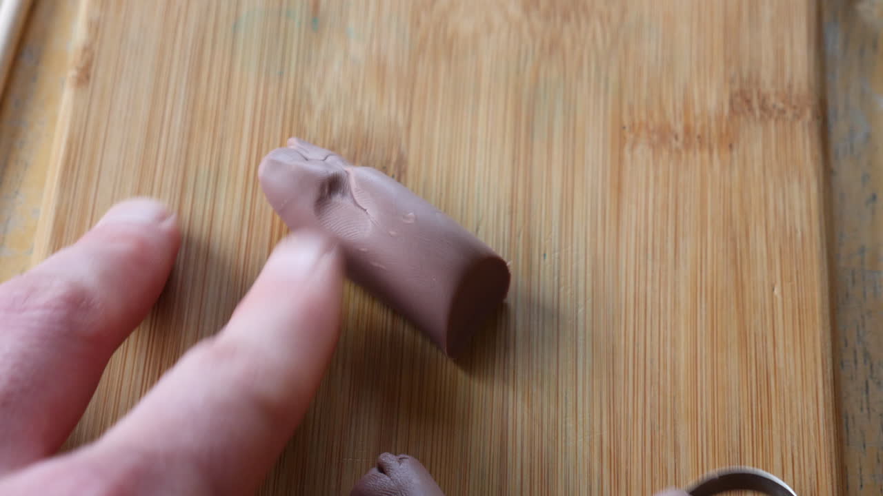 cerrar las manos de un artista o escultor cortando y tallando arcilla de modelado marrón suave con una herramienta de metal en un escritorio en un estudio de arte