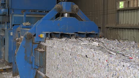 bale of shredded paper moves on conveyor belt out of baler at recycling center