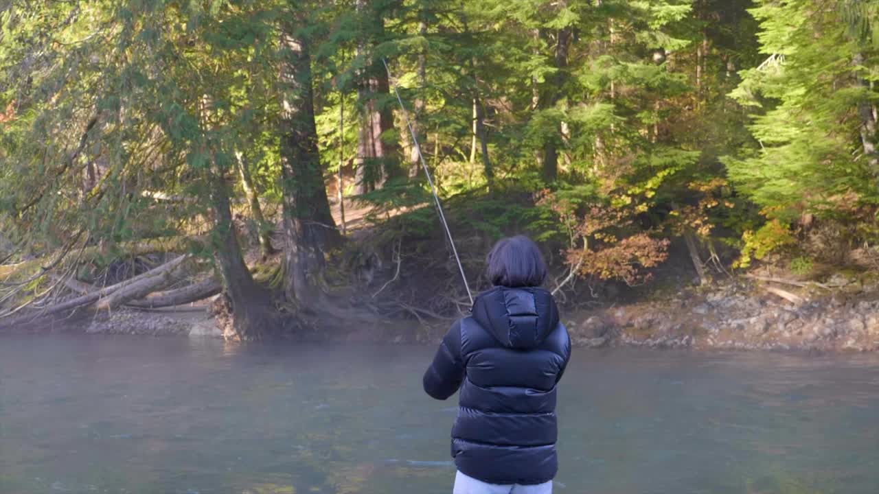 강 숲에서 복어 재킷 낚시를 입은 여성의 뒷모습