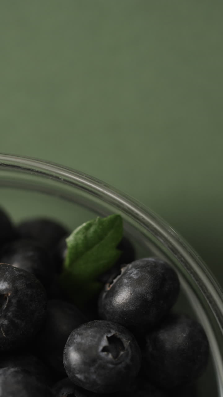 Micro vertical video close up of bowl of blueberries and copy space on green background
