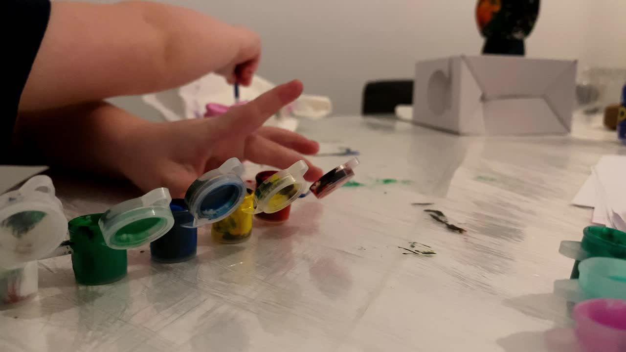 The child is holding the paint containers in his hand. The boy paints a small figure