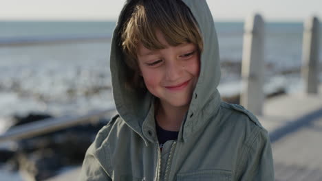 Primer-Plano-Retrato-Juguetón-Niño-Caucásico-Sonriendo-Feliz-Disfrutando-De-La-Playa-Con-Chaqueta-En-Un-Día-Ventoso-Y-Soleado-En-Cámara-Lenta