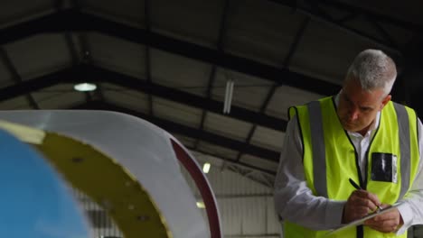 Male-engineer-writing-on-clipboard-in-hangar-4k