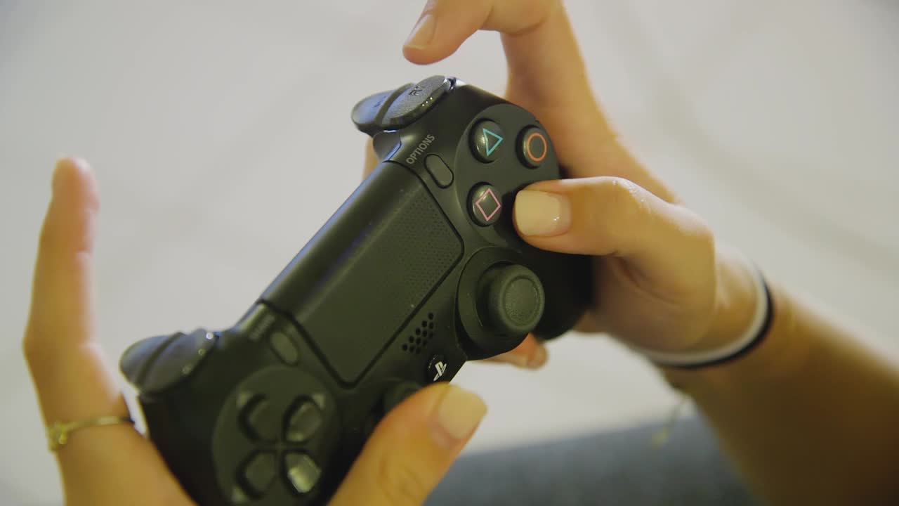 Closeup of female hands actively using black PS4 dualshock controller to play game inside home interior