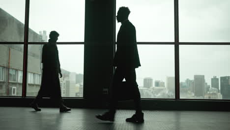 silhouettes of people walking in front of a city window