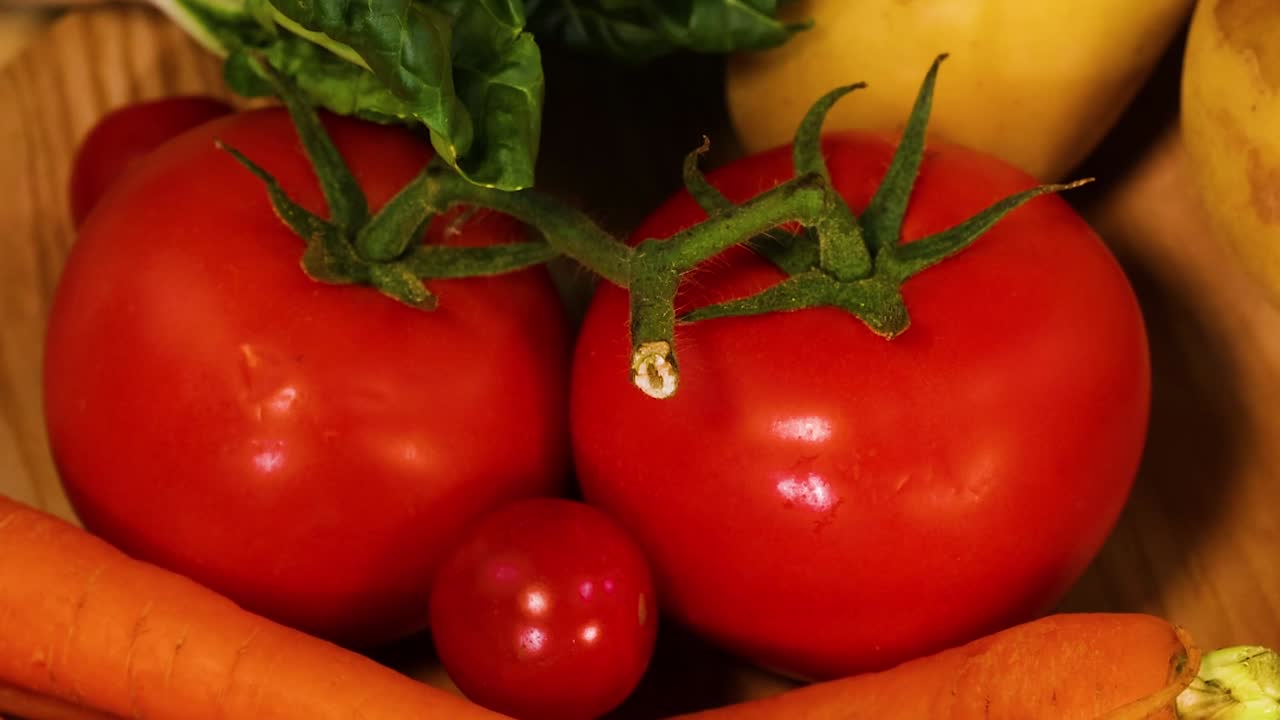 A colorful assortment of carrots, tomatoes, squash, and leafy greens arranged on a wooden surface.