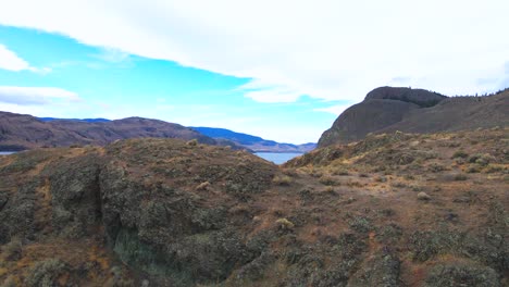 Cinematic-Scene-flying-reverse-over-grass-covered-hills-on-Kamloops-lake-on-a-partly-cloudy-day-in-the-autumn-in-a-desert-landscape-in-the-Nicola-Thompson-Region-in-BC-Canada