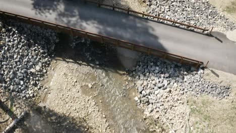 Aerial-drone-shot-of-a-fly-over-a-bridge-straight-down-to-tilt-up-to-reveal-creek