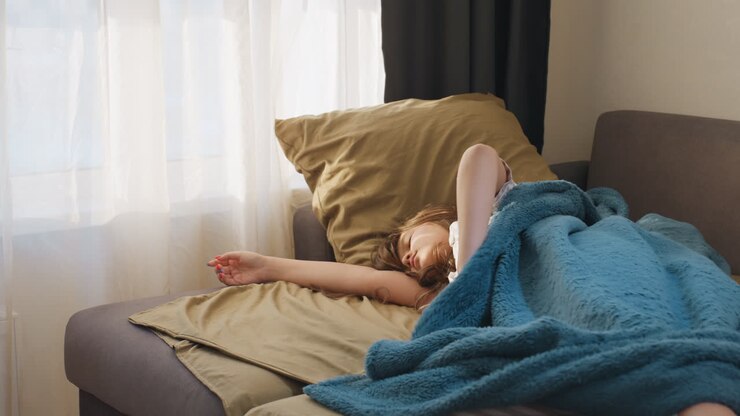 Træt kvinde slapper af på komfortabel sofa, udmattet kvinde læner sig tilbage i sofaen i blidt morgenlys, overanstrengt kvinde finder hvile i sofaen, mens morgensolen blidt filtreres ind