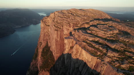 Impresionante-Vista-Aérea-De-Un-Impresionante-Acantilado-En-Noruega,-Atmósfera-Del-Amanecer-En-El-Fiordo-De-Lysefjorden,-Preikestolen,-Drones-Girando-Alrededor-De-La-Roca-Del-Púlpito-Con-Algunos-Turistas