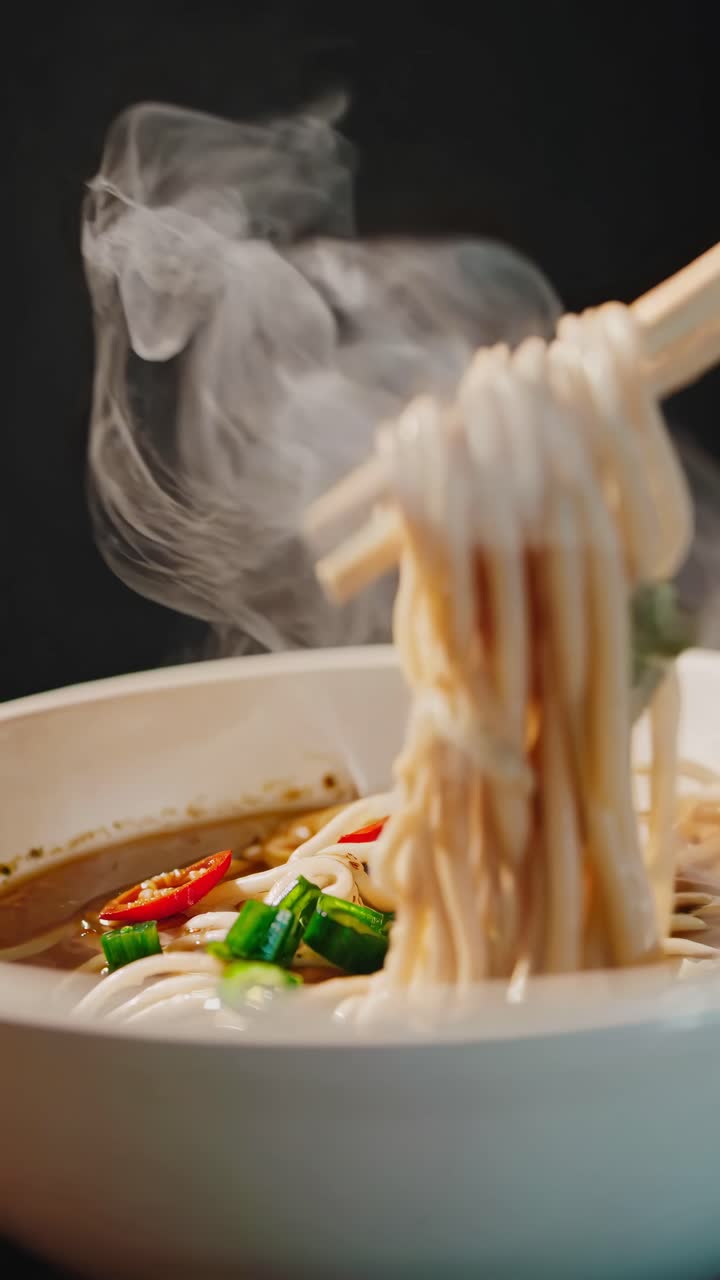 Close-up video of steaming noodles in a bowl, captured from a low angle, highlighting vibrant