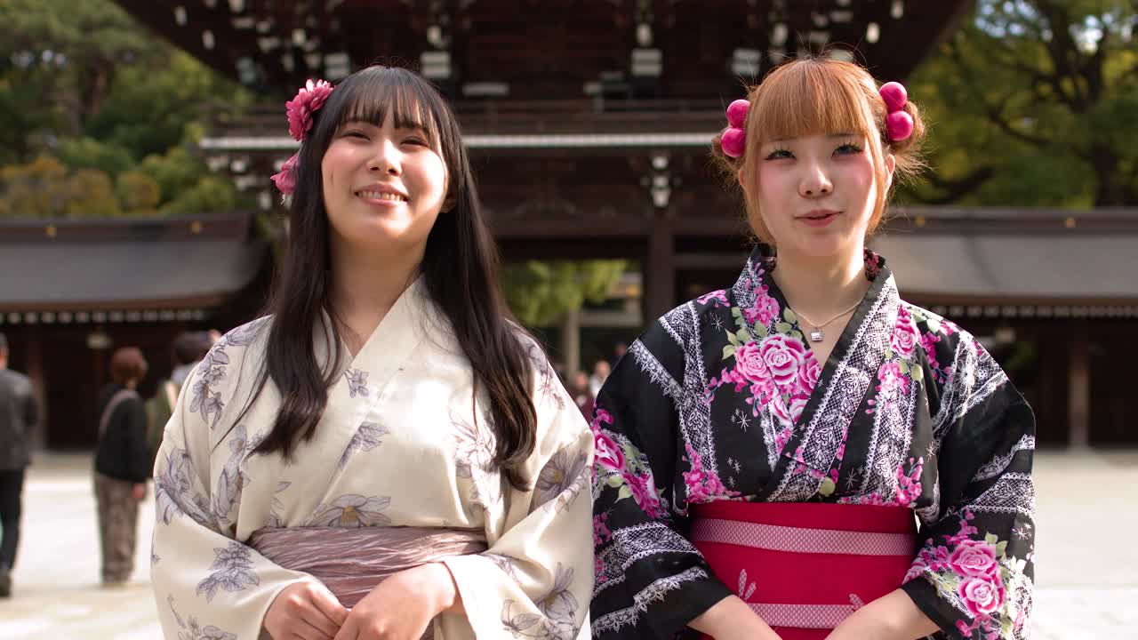Due donne che indossano kimono floreali stanno davanti a un santuario tradizionale alla luce naturale del giorno