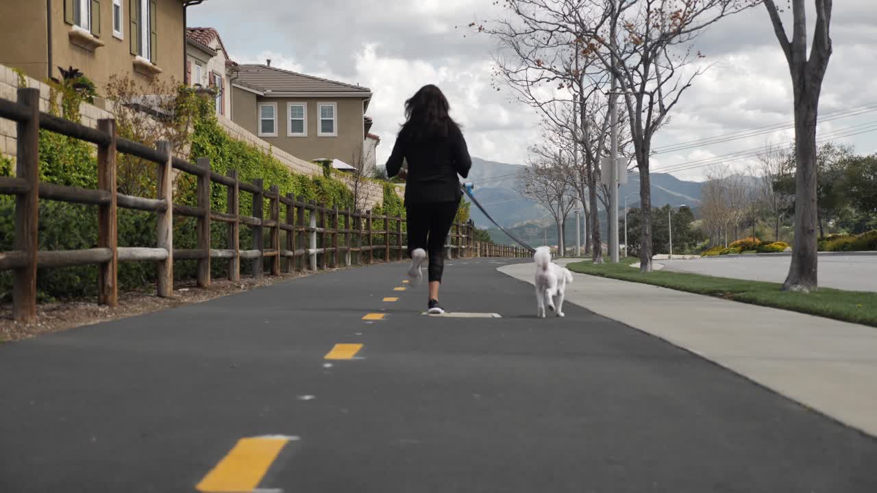 Woman jogging with pet Maltese dog on American walkway, lockdown, slow motion