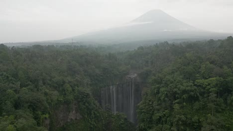 aerial rotates over misty, hazy tumpak sewu waterfall and java volcano