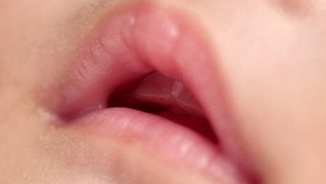 blurry close-up shot of the opened mouth of a sleeping newborn baby showing her pinkish lips and smooth skin