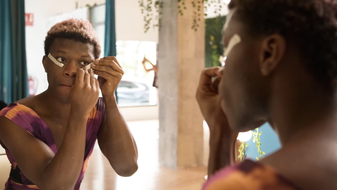 Uomo transgender africano che si applica strisce sul viso per truccarsi