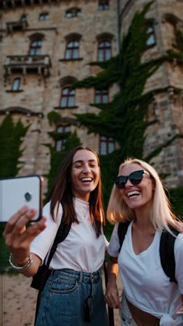 low-angle video shot of two women taking a selfie in front of a historic, ivy-covered castle