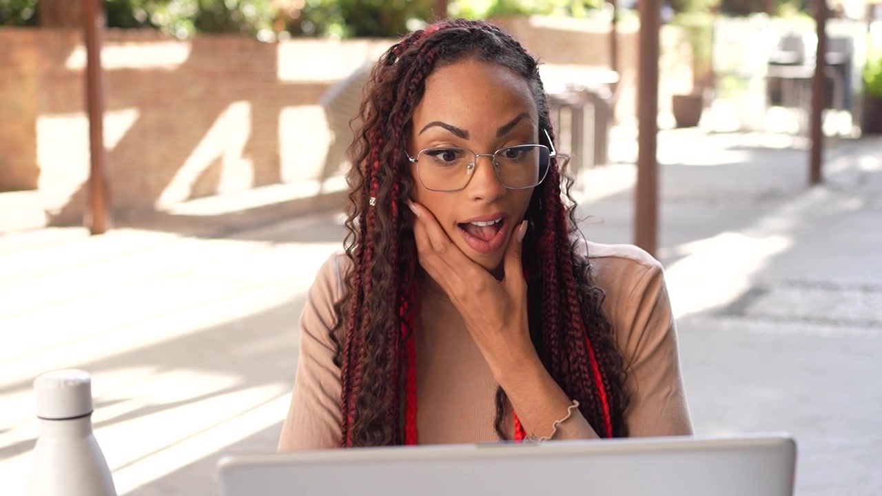 A bright and smiling young woman engaged in her work on a laptop while relishing the outdoors