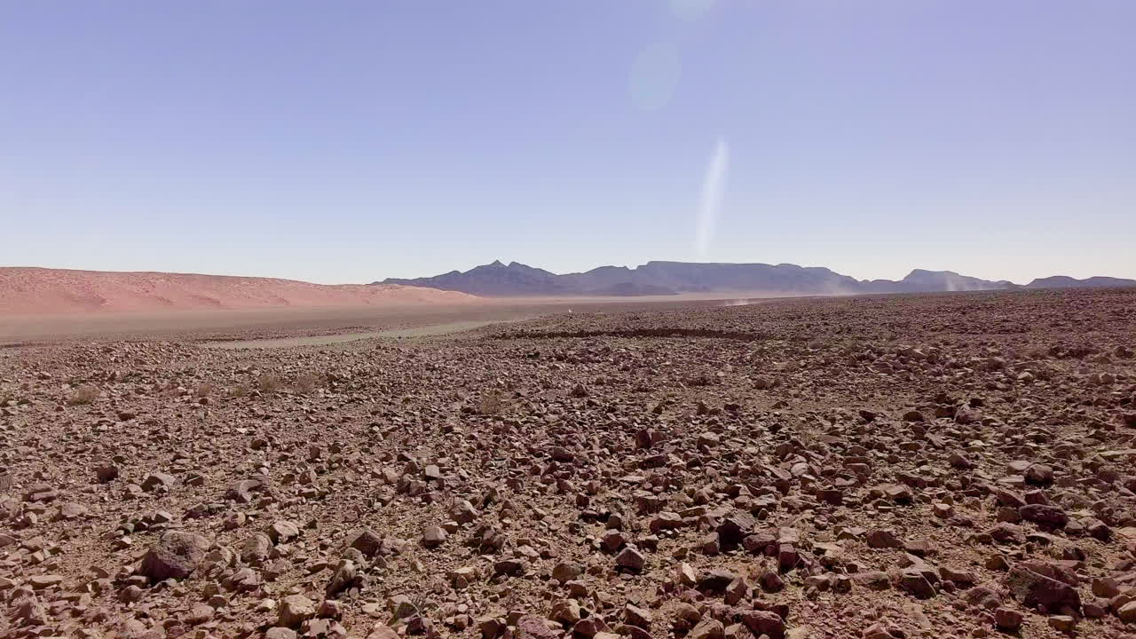 Flying low over rocky Namibian desert with car driving in distance, AERIAL