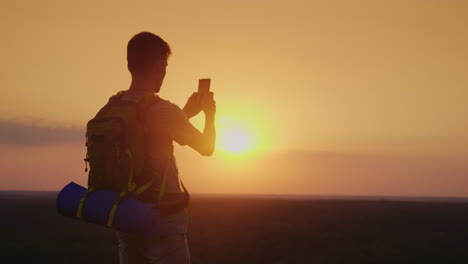 un joven con una mochila está tomando fotos de un hermoso paisaje al atardecer silueta en oran